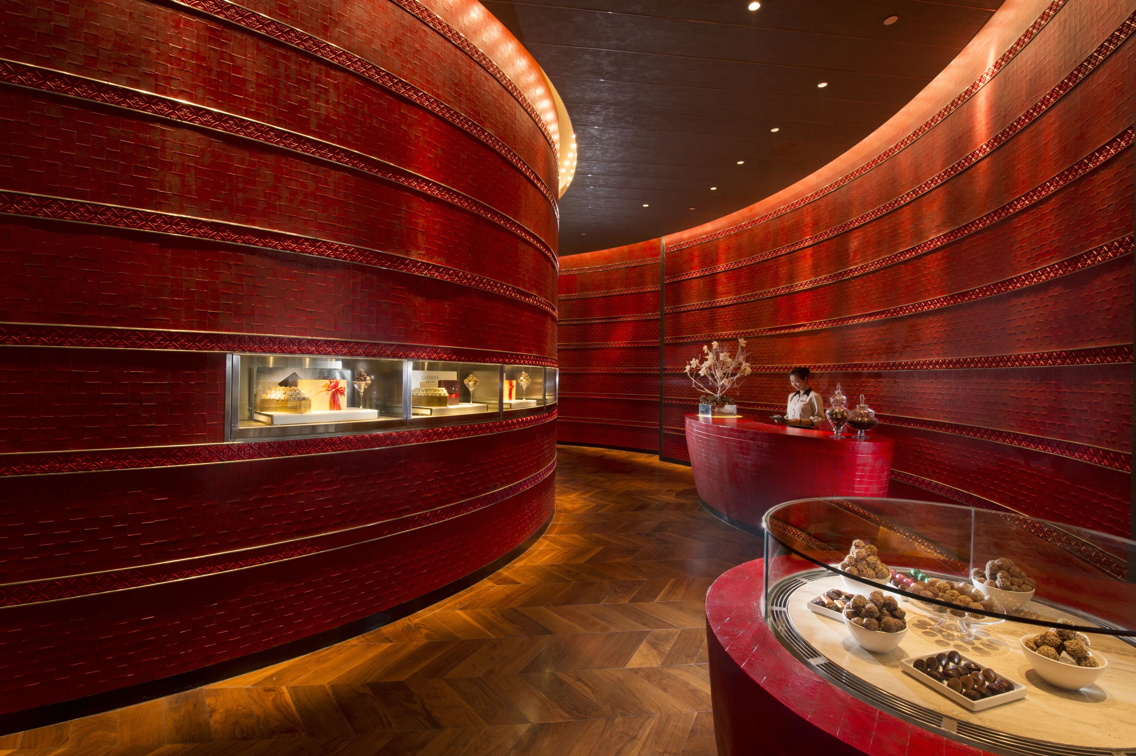 Een luxueuze lobby met vloeiende rode bakstenen muren, een gepolijste houten vloer en een glazen vitrine met chocolade.