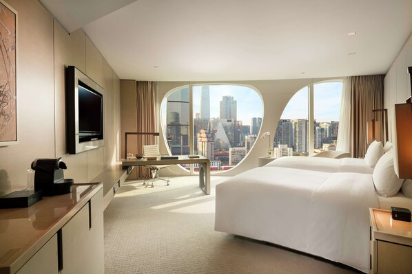 Una habitación de hotel moderna con una cama grande, un escritorio, una silla, un televisor y vistas a la ciudad.