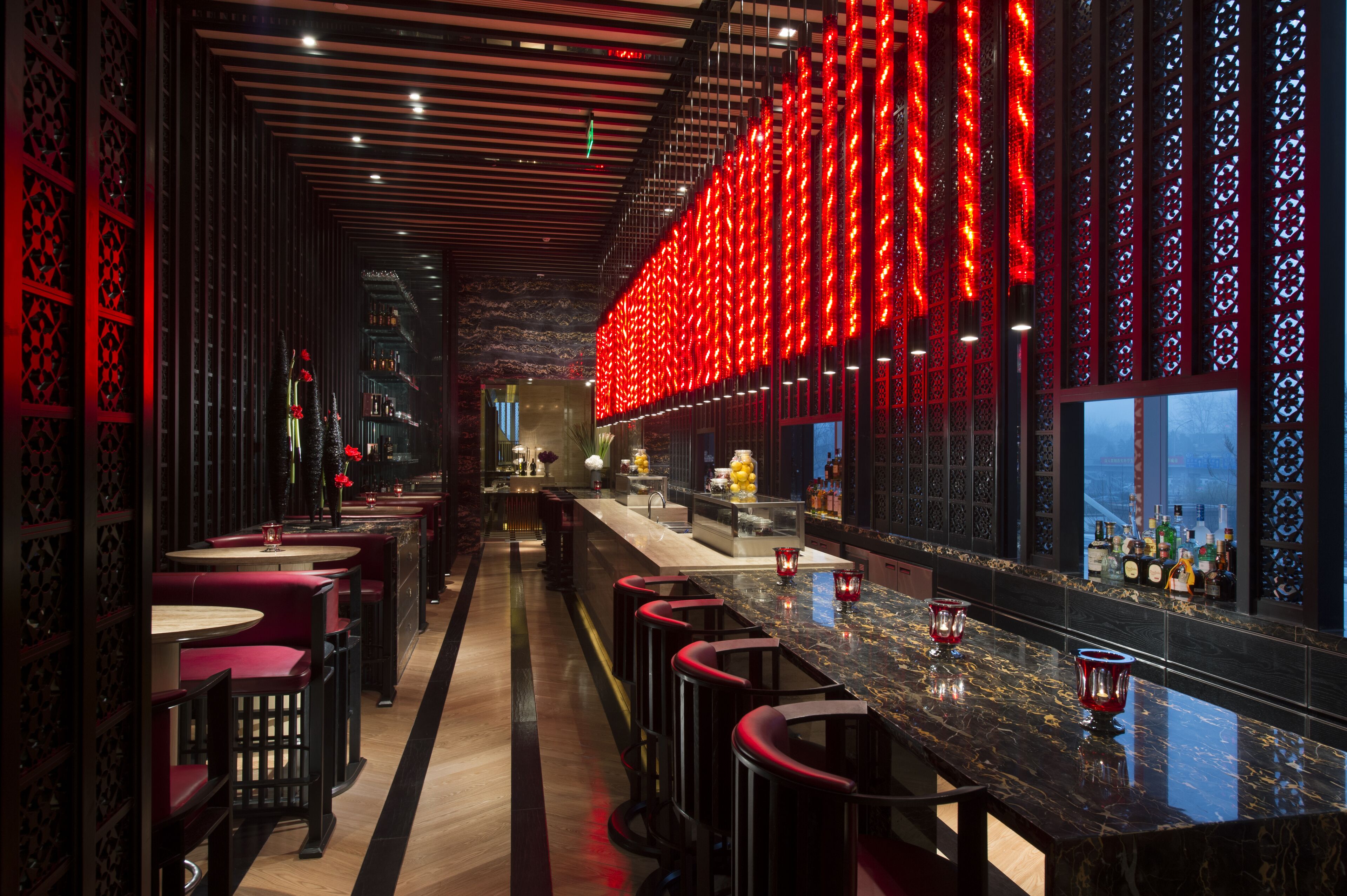 A bar area with red lighting, bar stools, and a long counter.