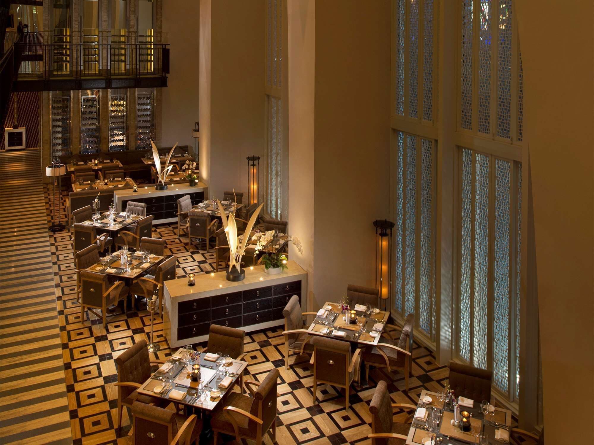 A spacious dining area with multiple tables and chairs, large windows with patterned glass, and a checkered floor.