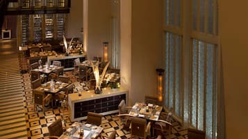 A spacious dining area with multiple tables and chairs, large windows with patterned glass, and a checkered floor.