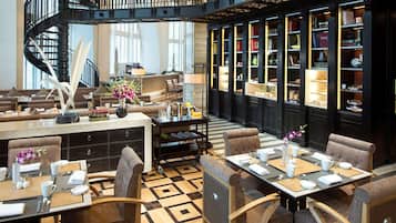 A hotel lobby with a central seating area, a staircase, and a bookcase filled with books.