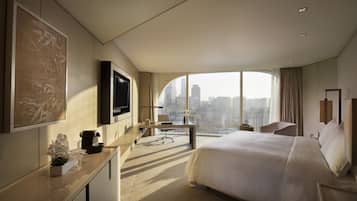 A modern hotel room with a large bed, a desk, a flat-screen TV, and a city view.