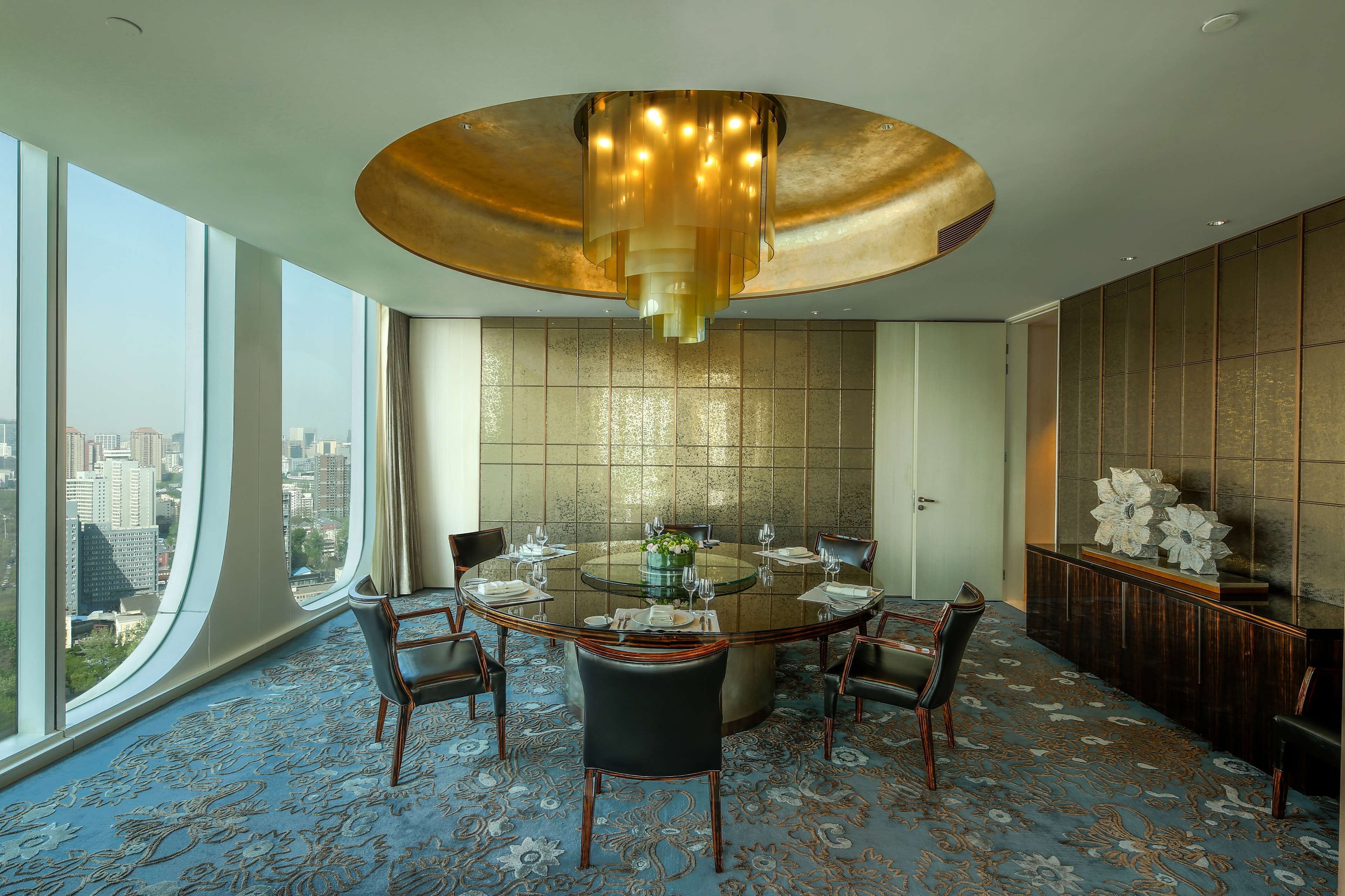 A modern dining room with a round glass table, black chairs, and a large gold chandelier.