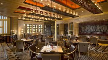 A spacious dining area with multiple tables and chairs, a patterned floor, and a modern chandelier.