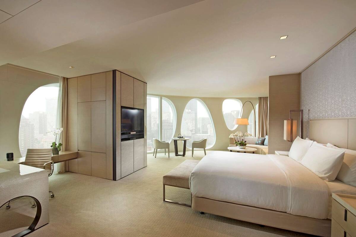 Ett modernt hotellrum med en stor säng, en TV, ett skrivbord och en sittgrupp med utsikt över staden.