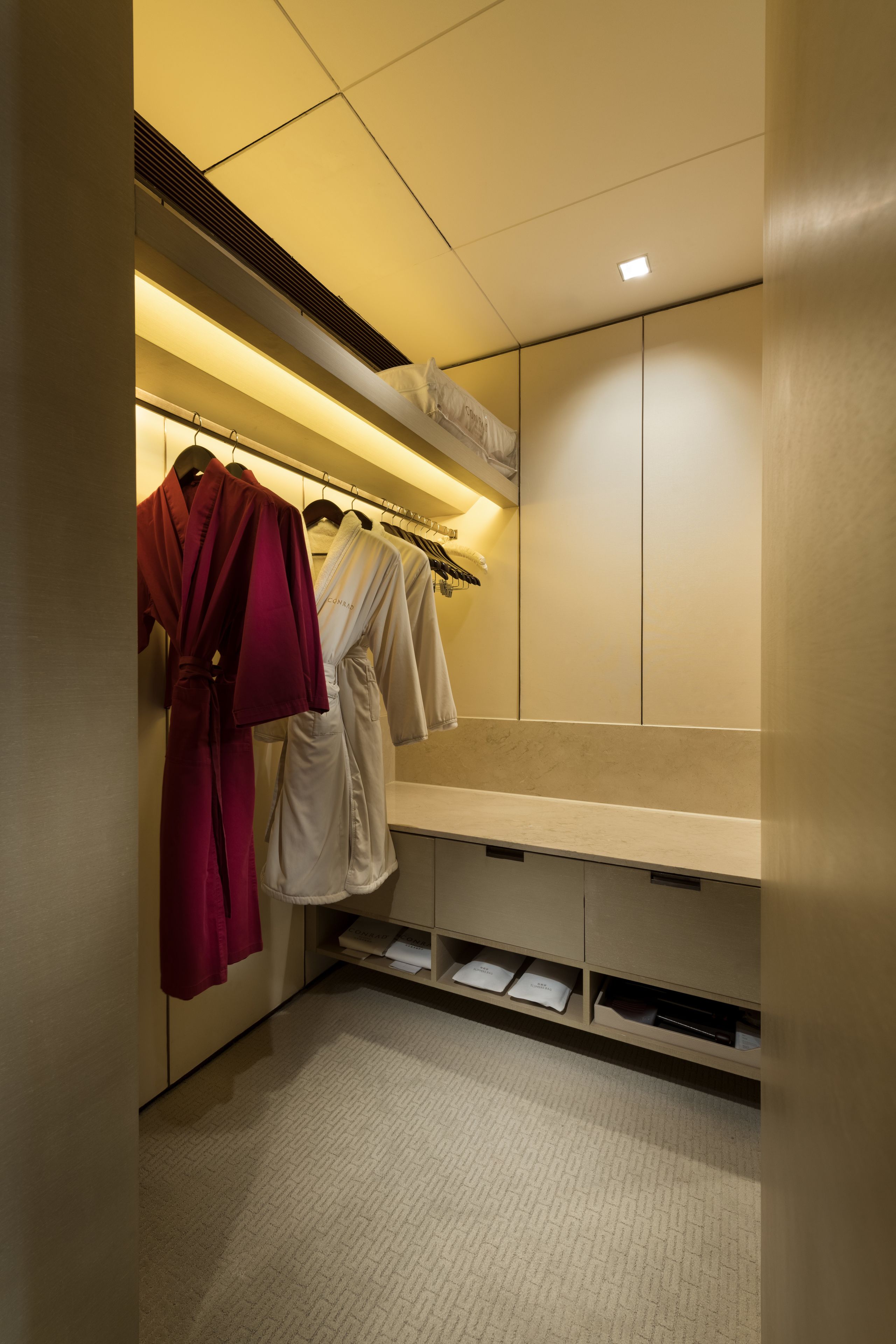 Habitación de hotel con un banco empotrado, un perchero para batas y un minibar.