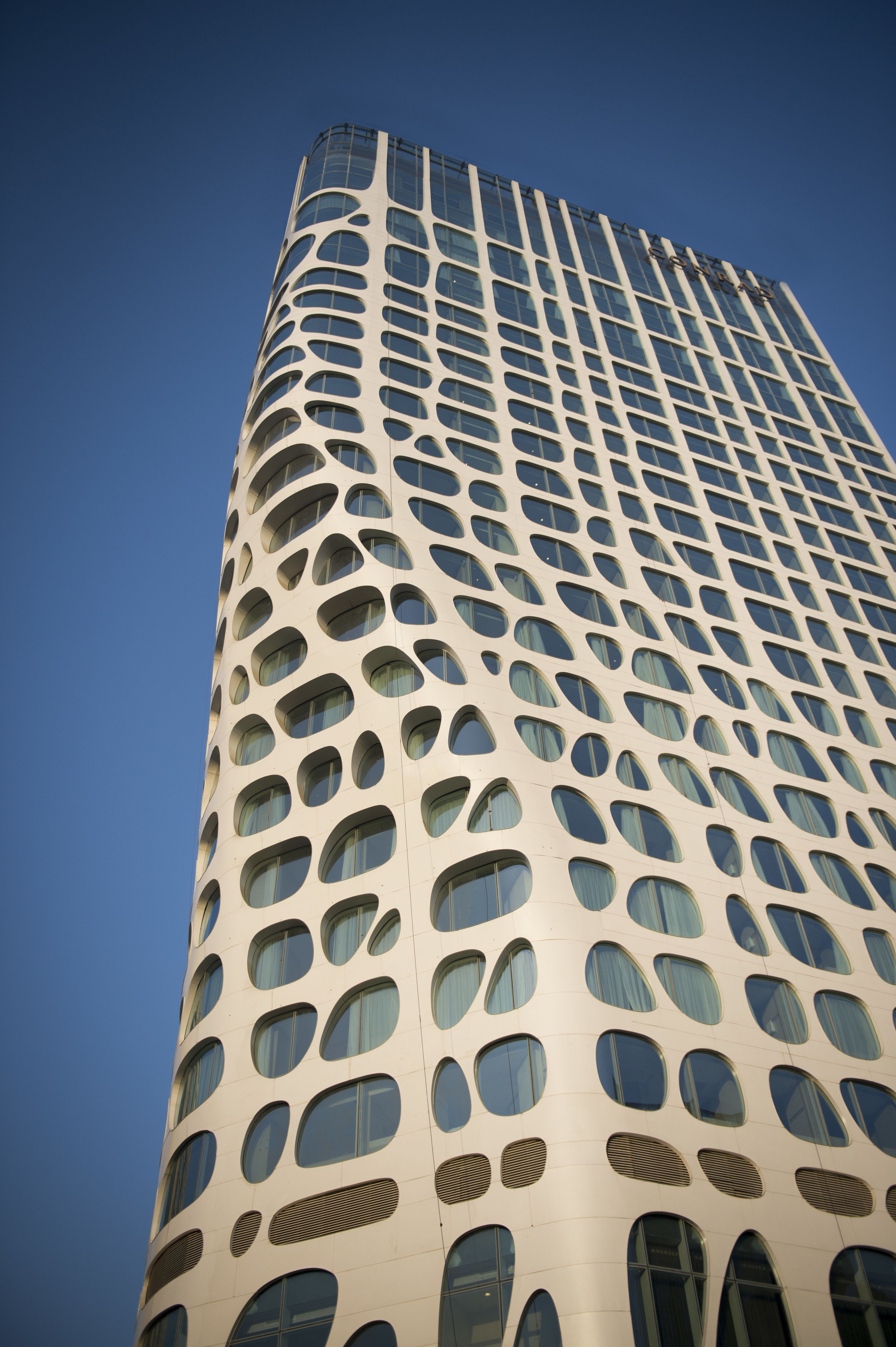 Um edifício alto com fachada distinta, apresentando um padrão repetitivo de janelas e painéis de ventilação.