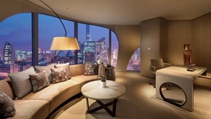 A modern hotel room with a curved sofa, a round table, a desk, and a large window offering a city view. - Conrad Beijing (Beijing)