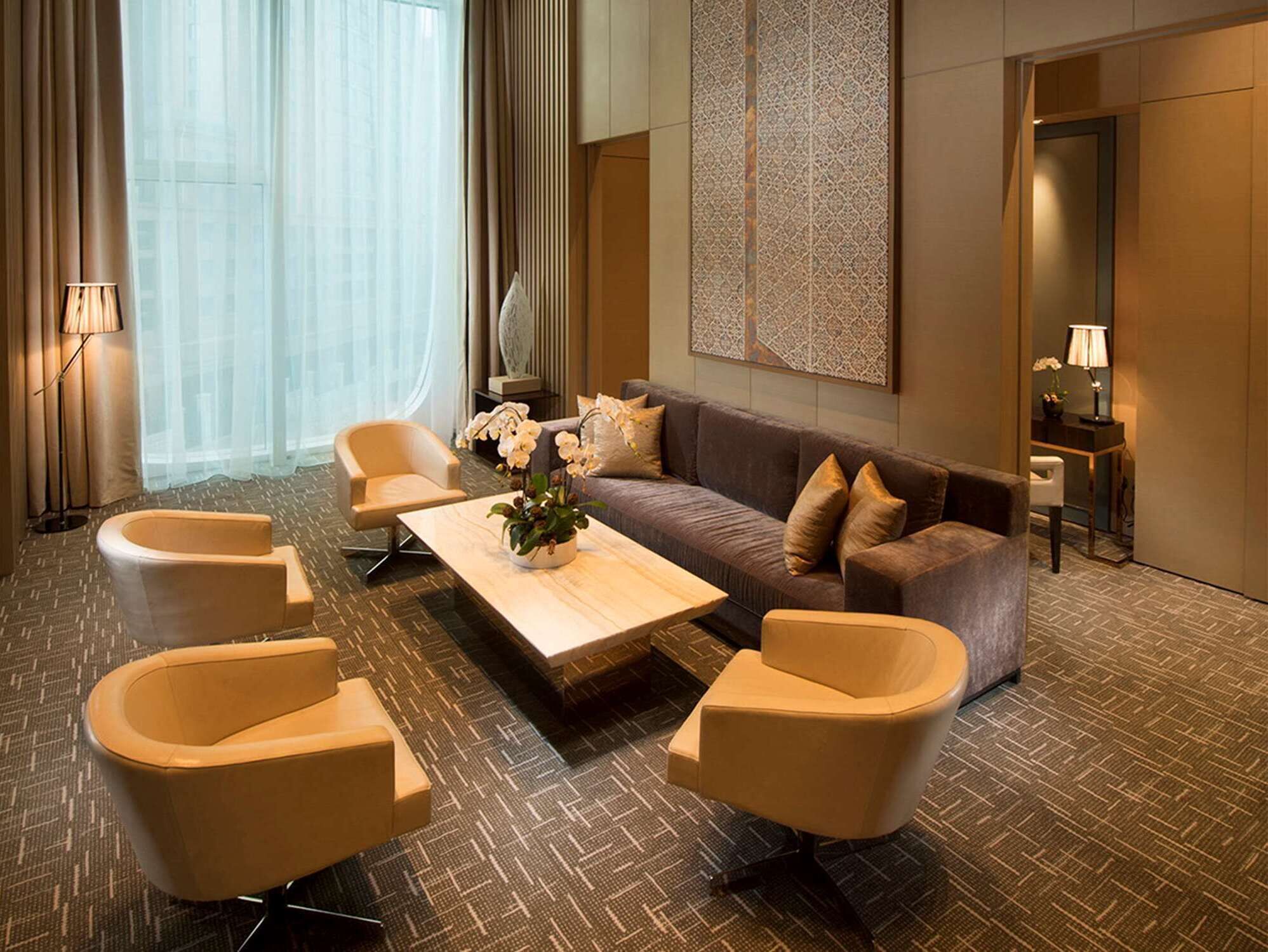 Una habitación de hotel moderna con un sofá, dos sillones, una mesita de centro y un elemento decorativo en la pared.