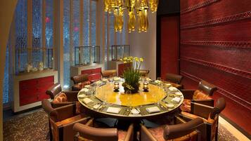 A round dining table with eight chairs, a chandelier, and a view through a mosaic window.