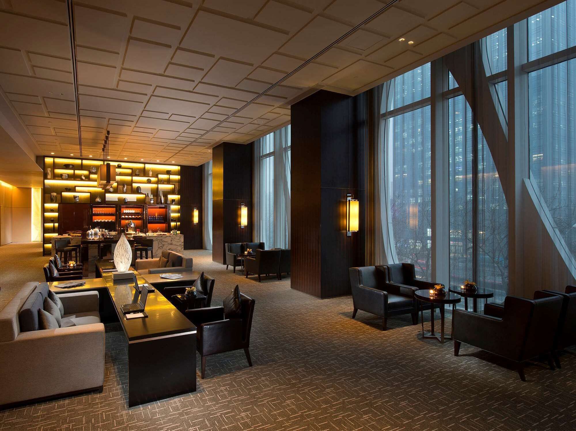 A modern hotel lobby with a reception desk, seating area, and large windows offering city views.