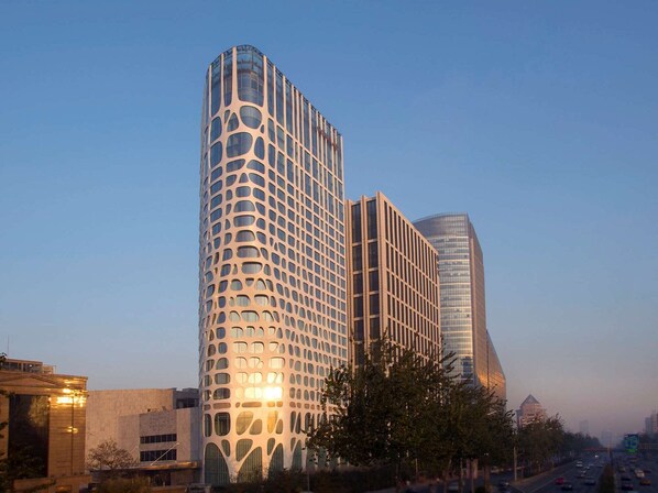 A modern high-rise building with a unique perforated facade, surrounded by other contemporary structures.