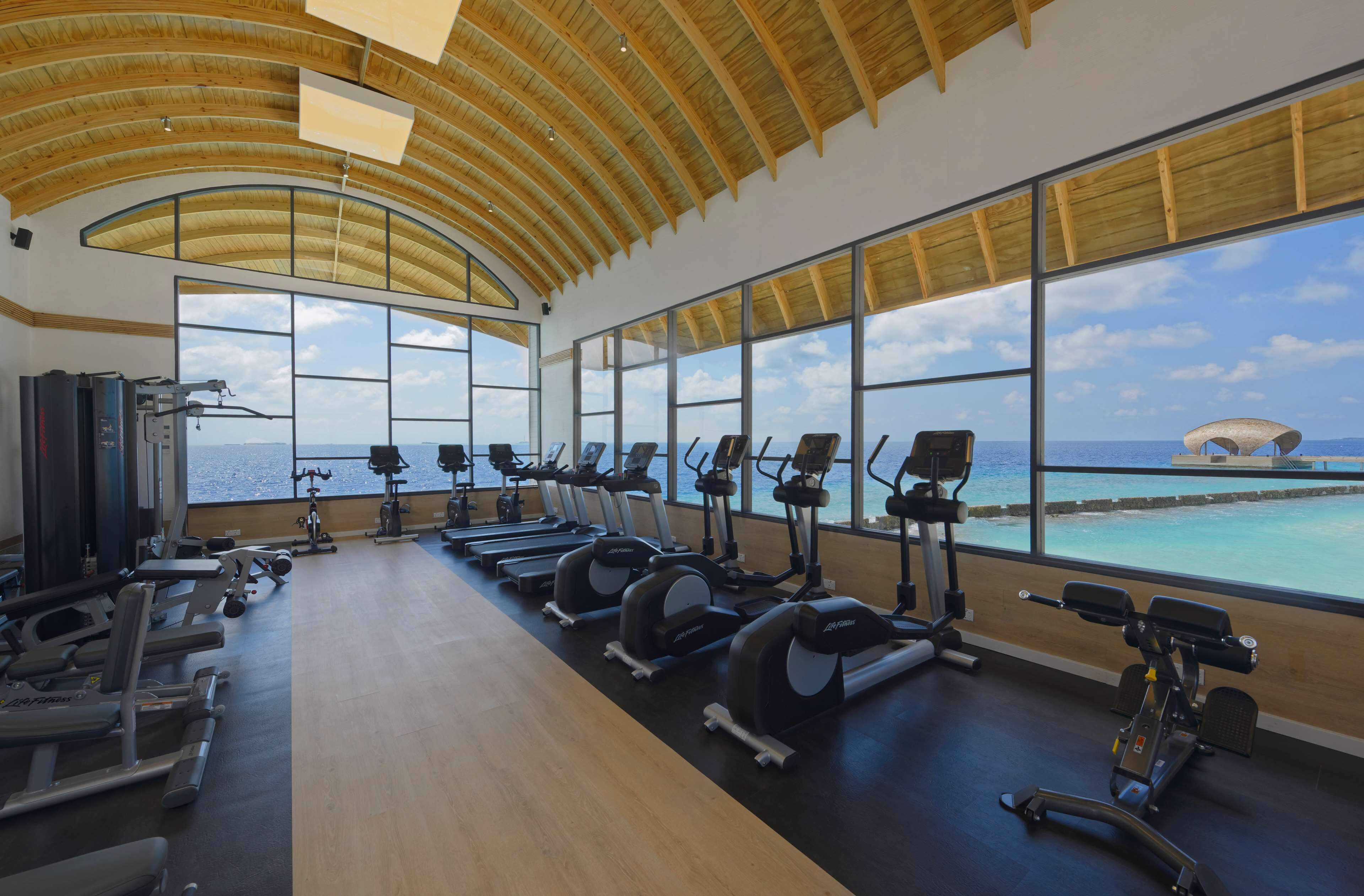A gym with exercise equipment, large windows, and a view of the ocean.