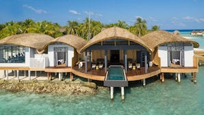 Cabañas sobre el agua con techos de paja, terrazas de madera y una piscina.