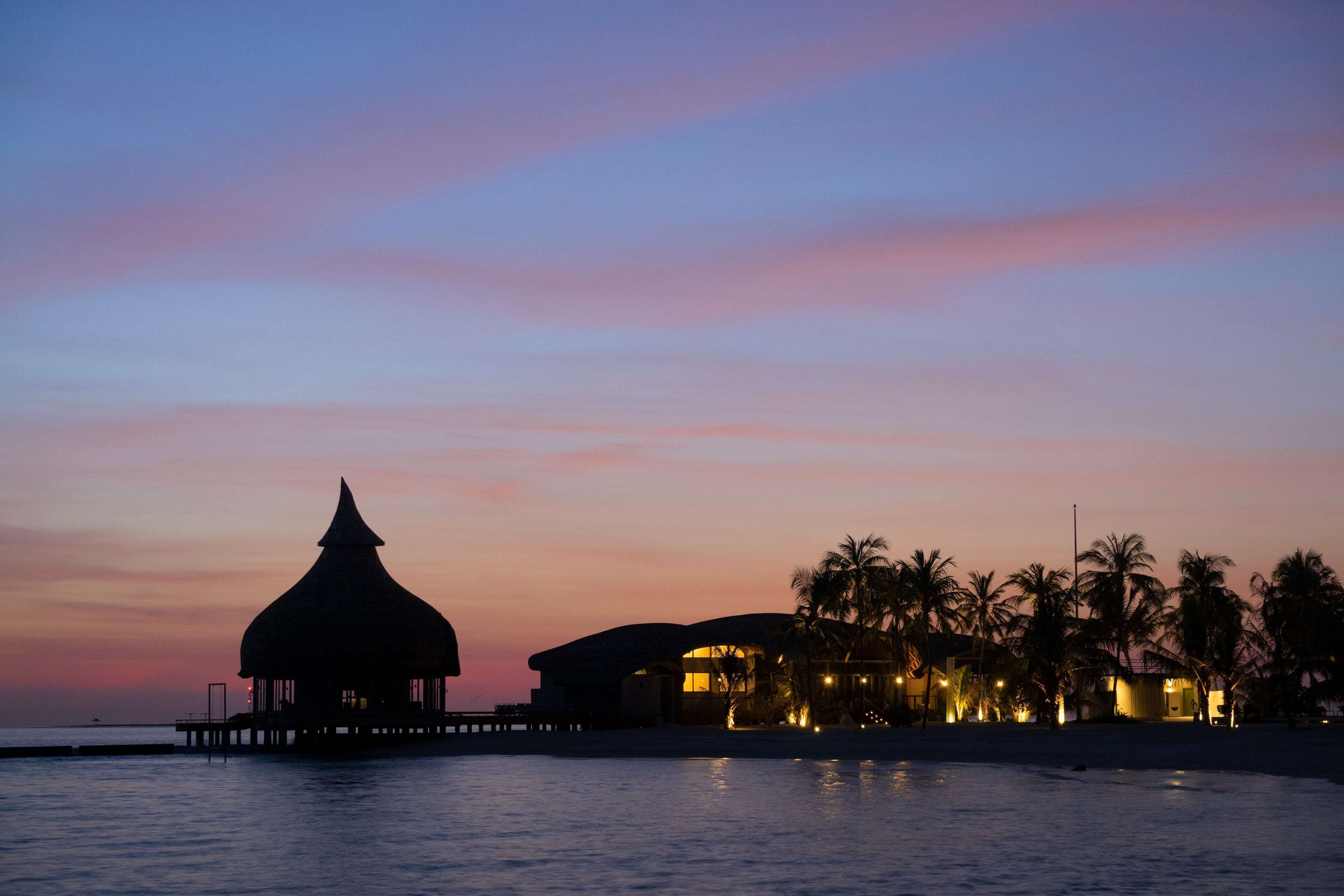A resort with overwater bungalows, palm trees, and a sunset sky.