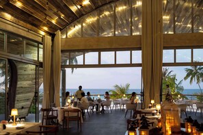 A restaurant with tables and chairs, large windows, and a view of the ocean.