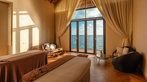 Una habitación con una cama, un sofá, una mesita y una silla, con vistas al mar a través de amplios ventanales.