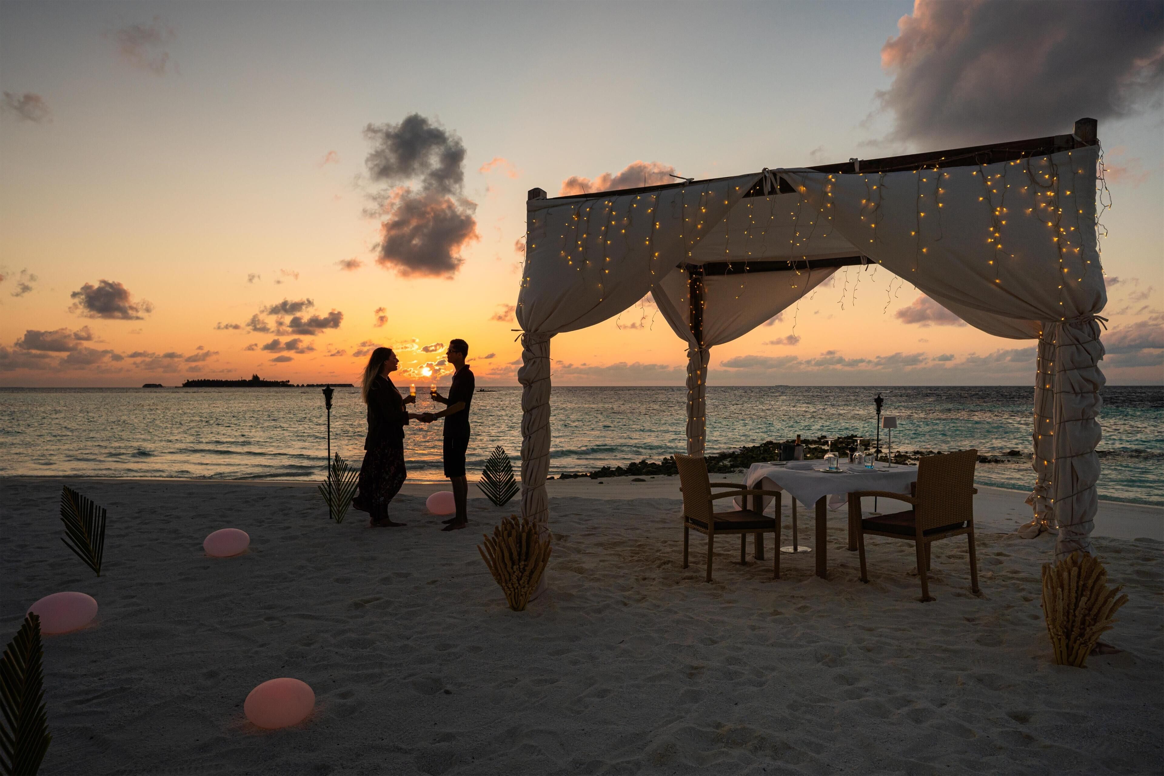 A beachside setting with a canopy, chairs, and a table, suggesting a romantic outdoor dining area.