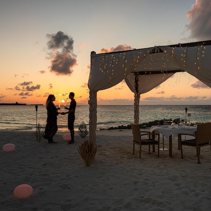 A beachside setting with a canopy, chairs, and a table, suggesting a romantic outdoor dining area.