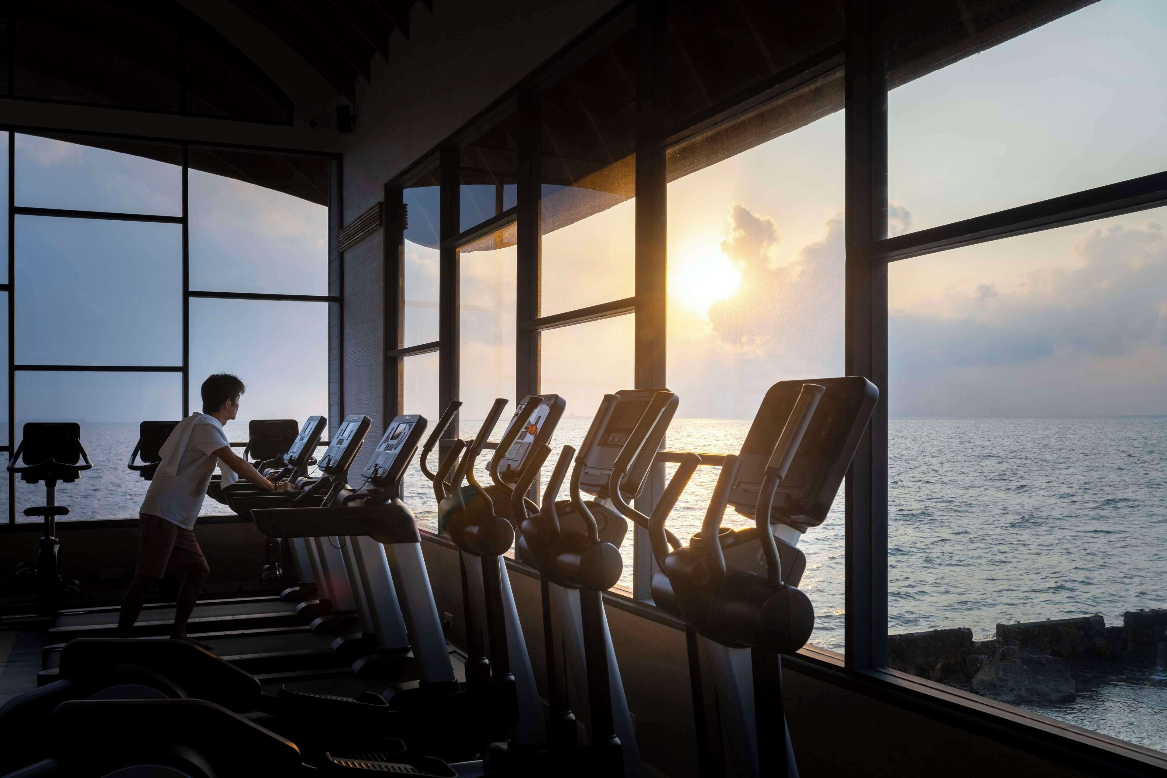 A gym with treadmills and exercise equipment, large windows with a view of the sea.