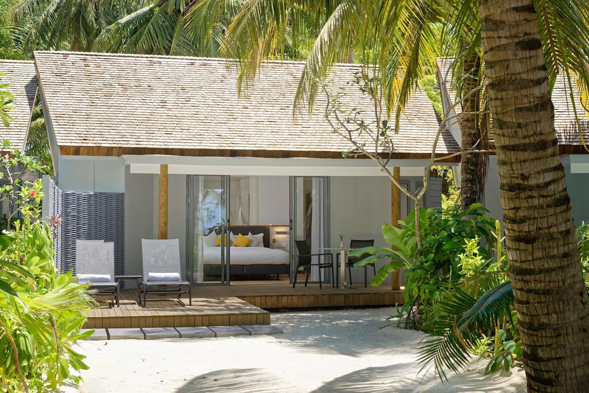 A modern, single-story building with a bedroom, a balcony, and a small outdoor seating area.