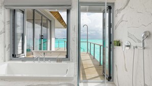 A modern bathroom with a large bathtub, a glass-enclosed shower area, and a view of the ocean.