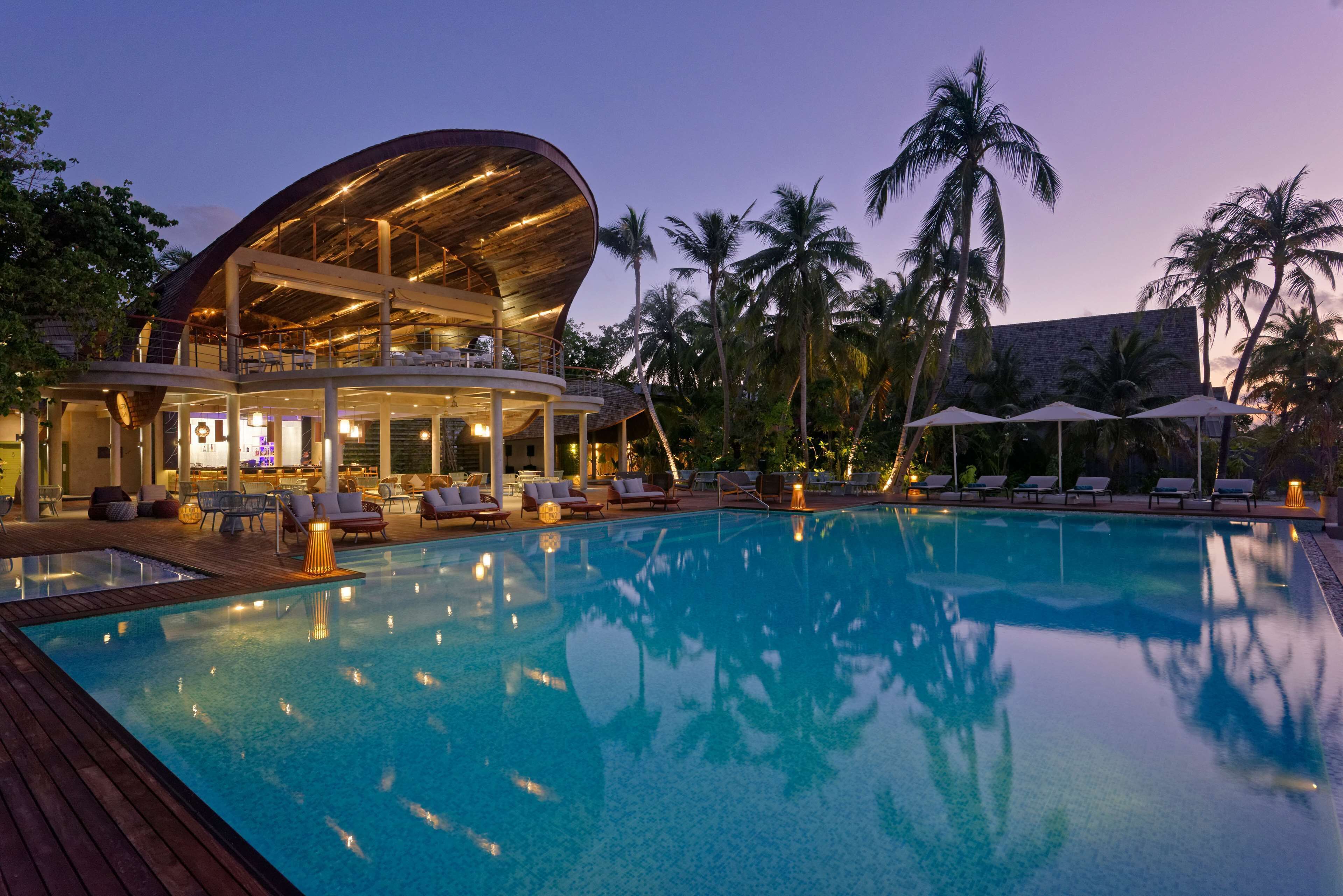 Ein modernes Hotel mit Pool, Liegestühlen und Palmen.