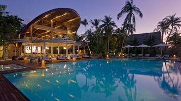 Ein modernes Hotel mit Pool, Liegestühlen und Palmen.