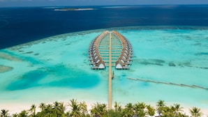 Vista aérea de un resort con bungalows sobre el agua, unidos por una pasarela de madera.
