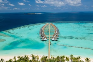 An aerial view of a resort with overwater bungalows connected by a wooden walkway.