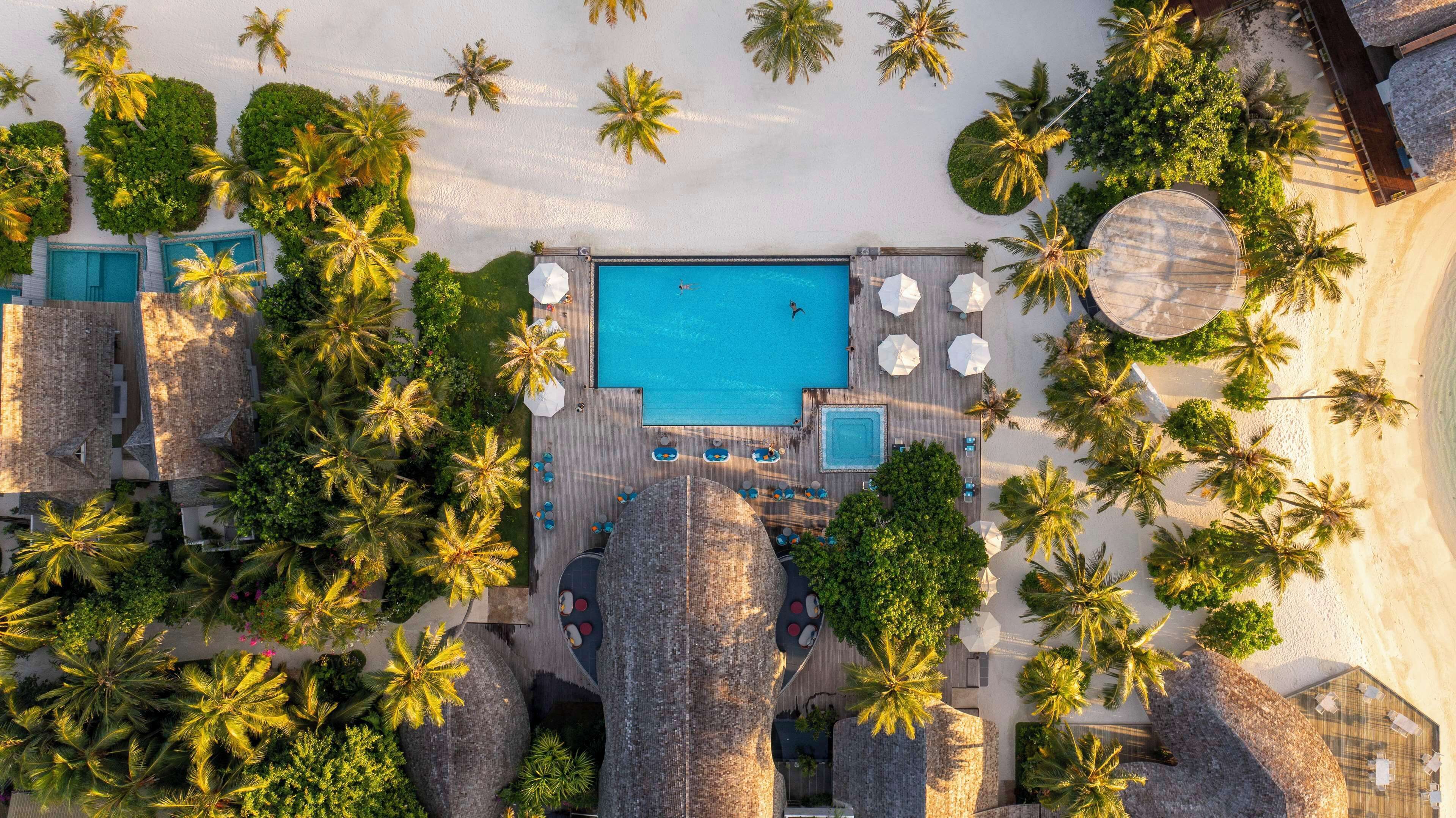 Vista aérea de un resort con piscina central, rodeado de palmeras y estructuras de techo de paja.