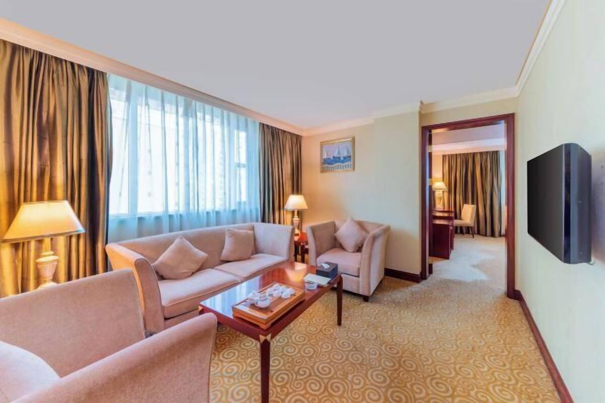 Une chambre d’hôtel équipée d’un canapé, d’un fauteuil, d’une table basse, d’une télévision et d’un tapis à motifs.