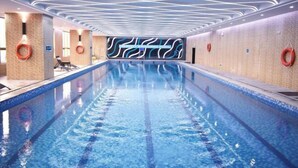 Uma piscina interior moderna com design geométrico no teto, água cristalina e boias de segurança nas paredes.