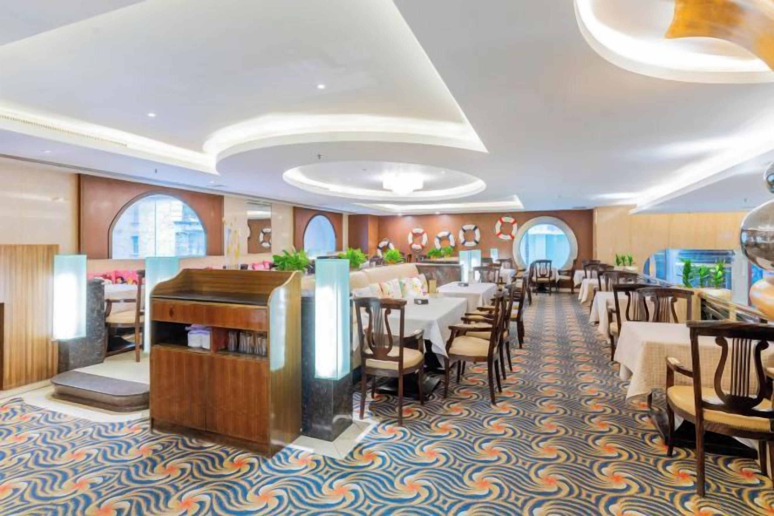 Une salle à manger d’hôtel spacieuse, dotée de nombreuses tables et chaises, d’un comptoir central et d’un sol à motifs.