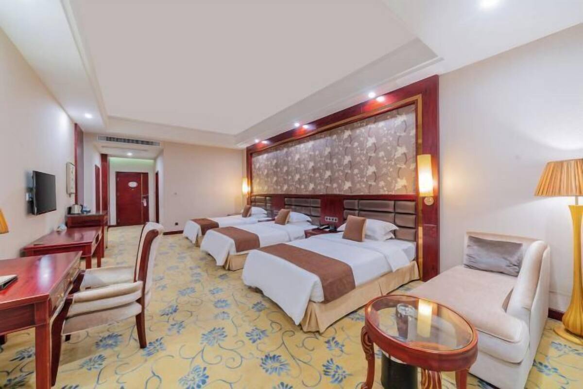 Une chambre d’hôtel avec trois lits, un canapé, un bureau et une télévision.