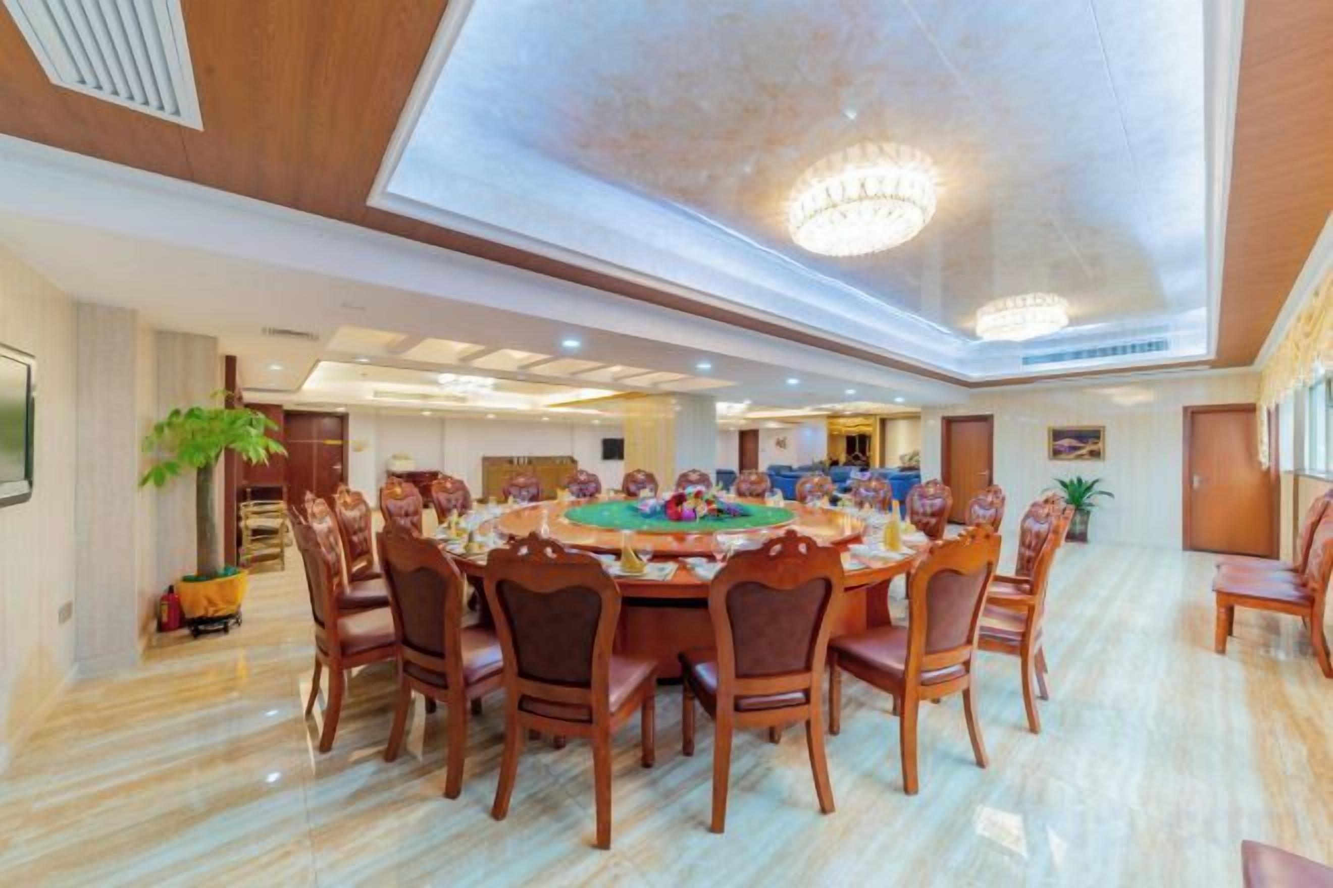 A spacious dining area with a large round table surrounded by chairs, a chandelier, and a view of the sky through the ceiling.