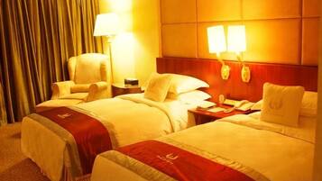 A hotel room with two beds, a nightstand with a lamp, a chair, and a headboard with wall-mounted lamps.