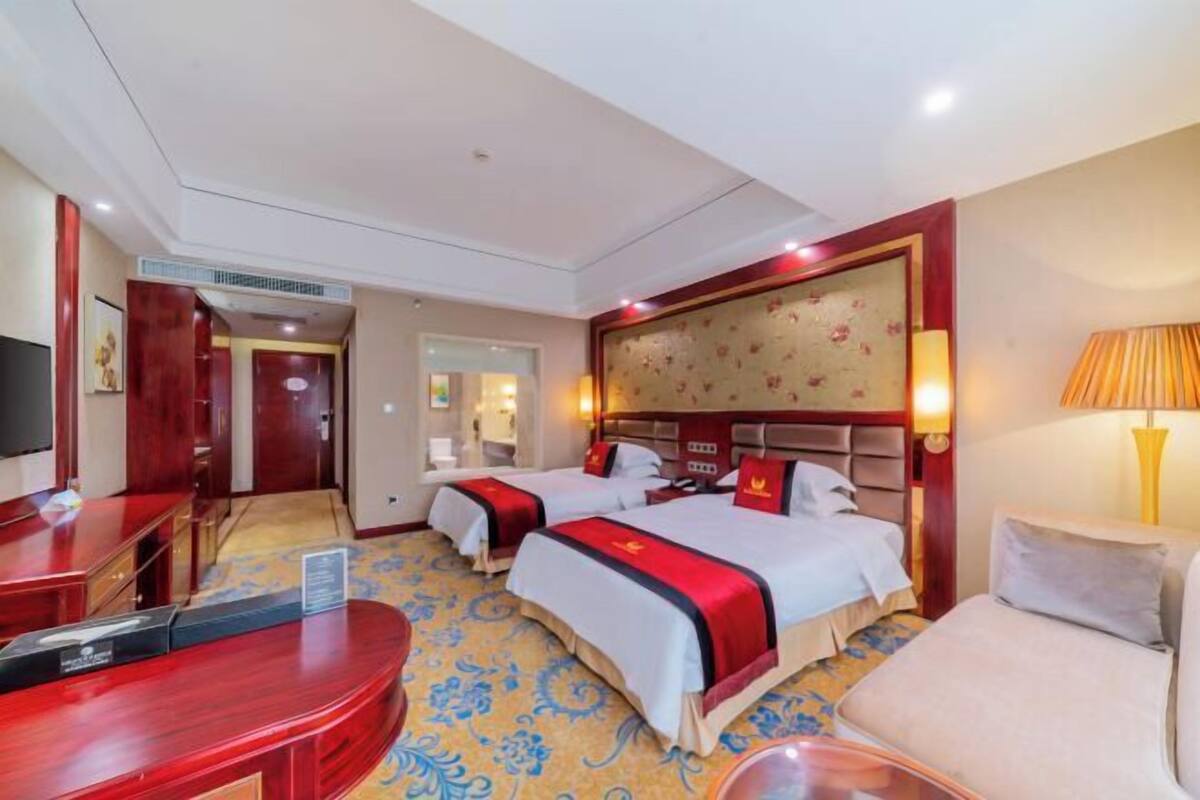 Une chambre d’hôtel avec deux lits, un bureau, une chaise, une télévision et une lampe.