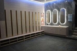 A modern bathroom with a wooden bench, a vanity with a mirror, and a marble wall. - Hotel de Royce (Shaoguan)