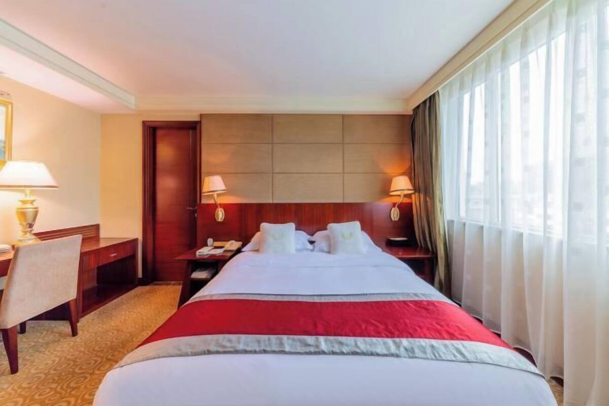Une chambre d’hôtel avec un lit, un bureau, une chaise, une table de chevet et une fenêtre avec des rideaux.