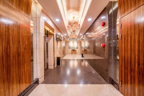 A hotel corridor with a chandelier, wooden paneling, and a polished floor. - Hotel de Royce (Shaoguan)