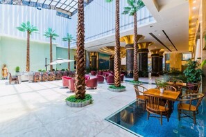 Un amplio espacio interior con piscina, áreas de descanso y altas palmeras.