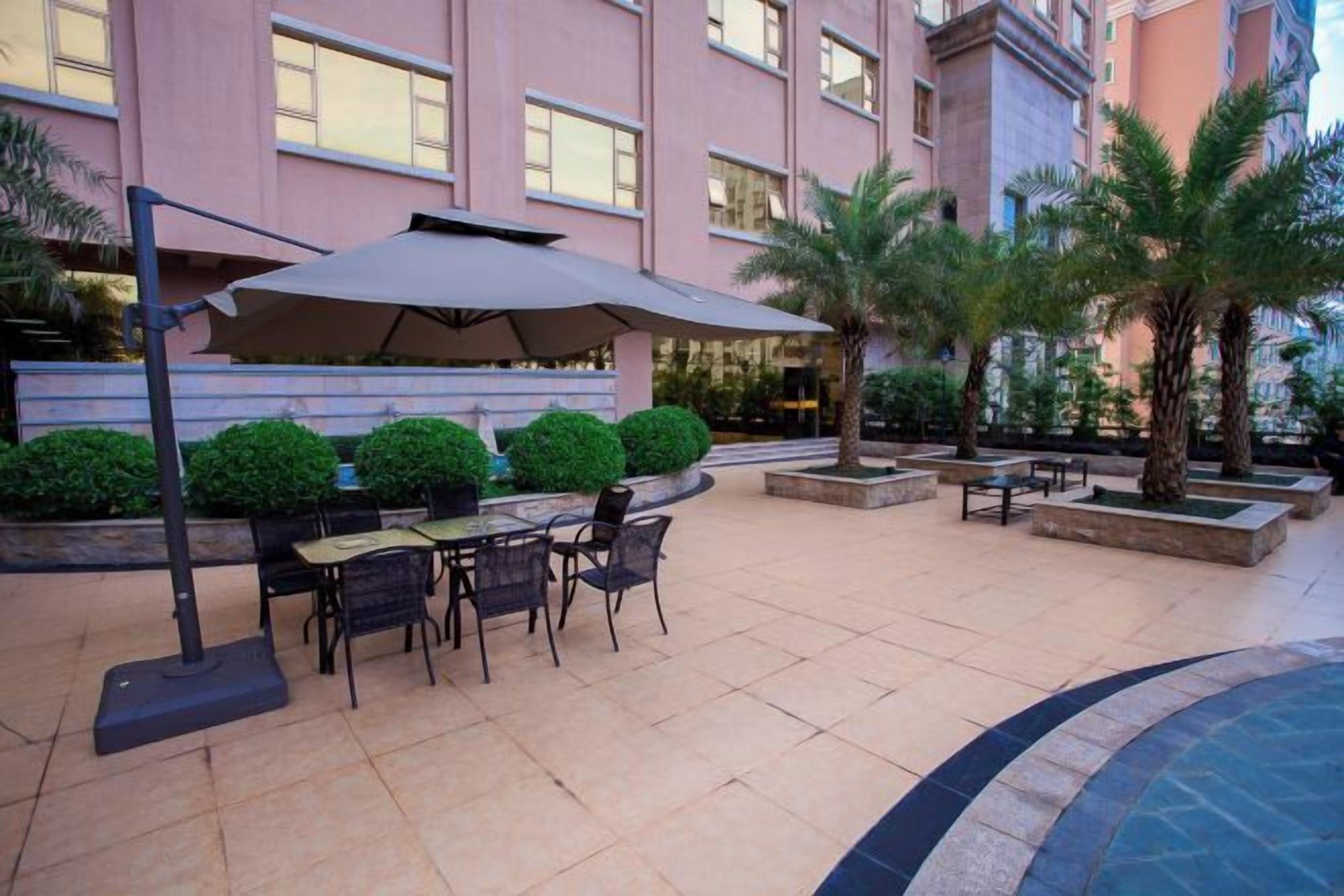 An outdoor patio with a table and chairs, surrounded by planters and palm trees.