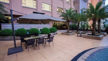 An outdoor patio with a table and chairs, surrounded by planters and palm trees.