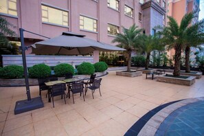 An outdoor patio with a table and chairs, surrounded by planters and palm trees. - Hotel de Royce (Shaoguan)