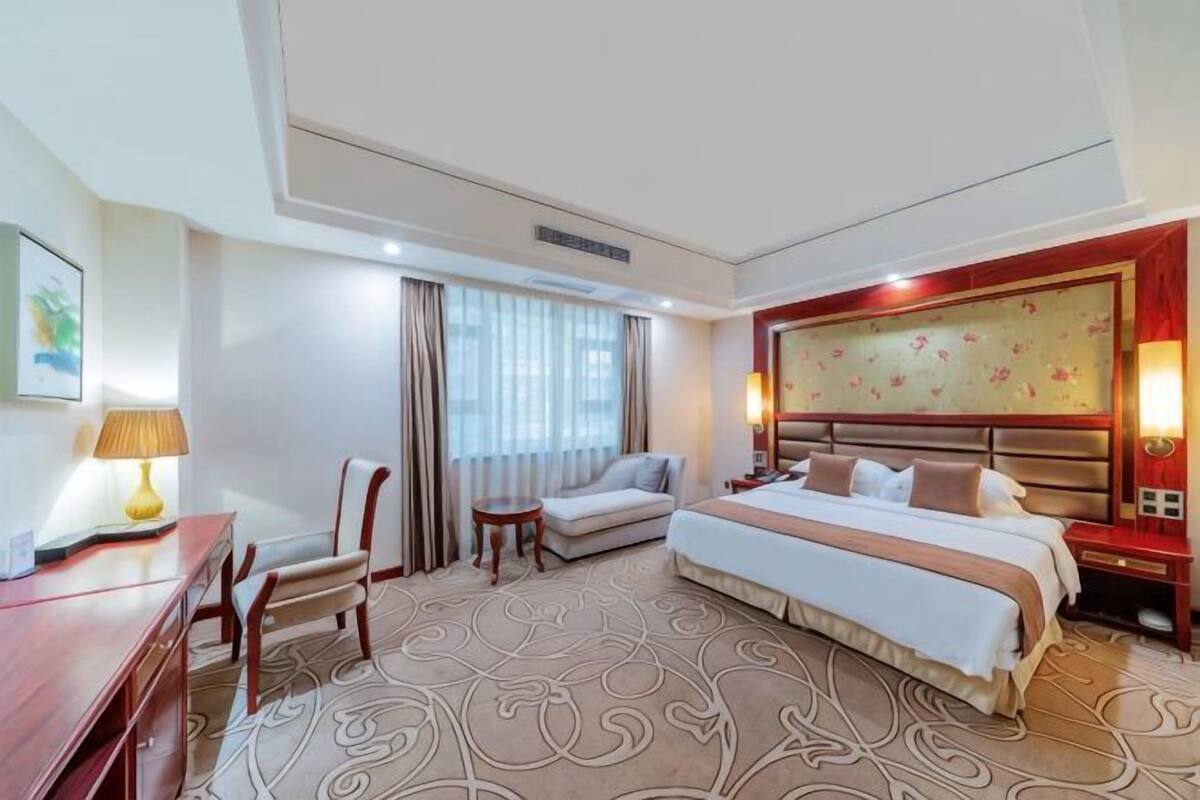 Une chambre d’hôtel avec un lit, un bureau, une chaise, un canapé et une fenêtre avec des rideaux.