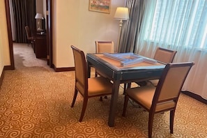 A hotel room with a dining table, four chairs, a lamp, a painting, and a patterned carpet. - Hotel de Royce (Shaoguan)