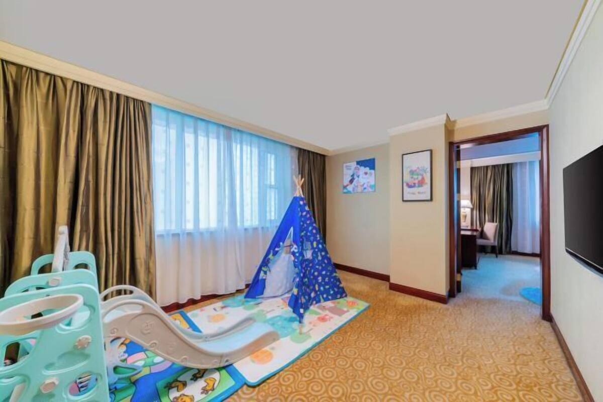 Une chambre d’hôtel dotée d’un espace de jeux, comprenant un parc pour enfants et une petite tente, ainsi qu’un sol recouvert de moquette.