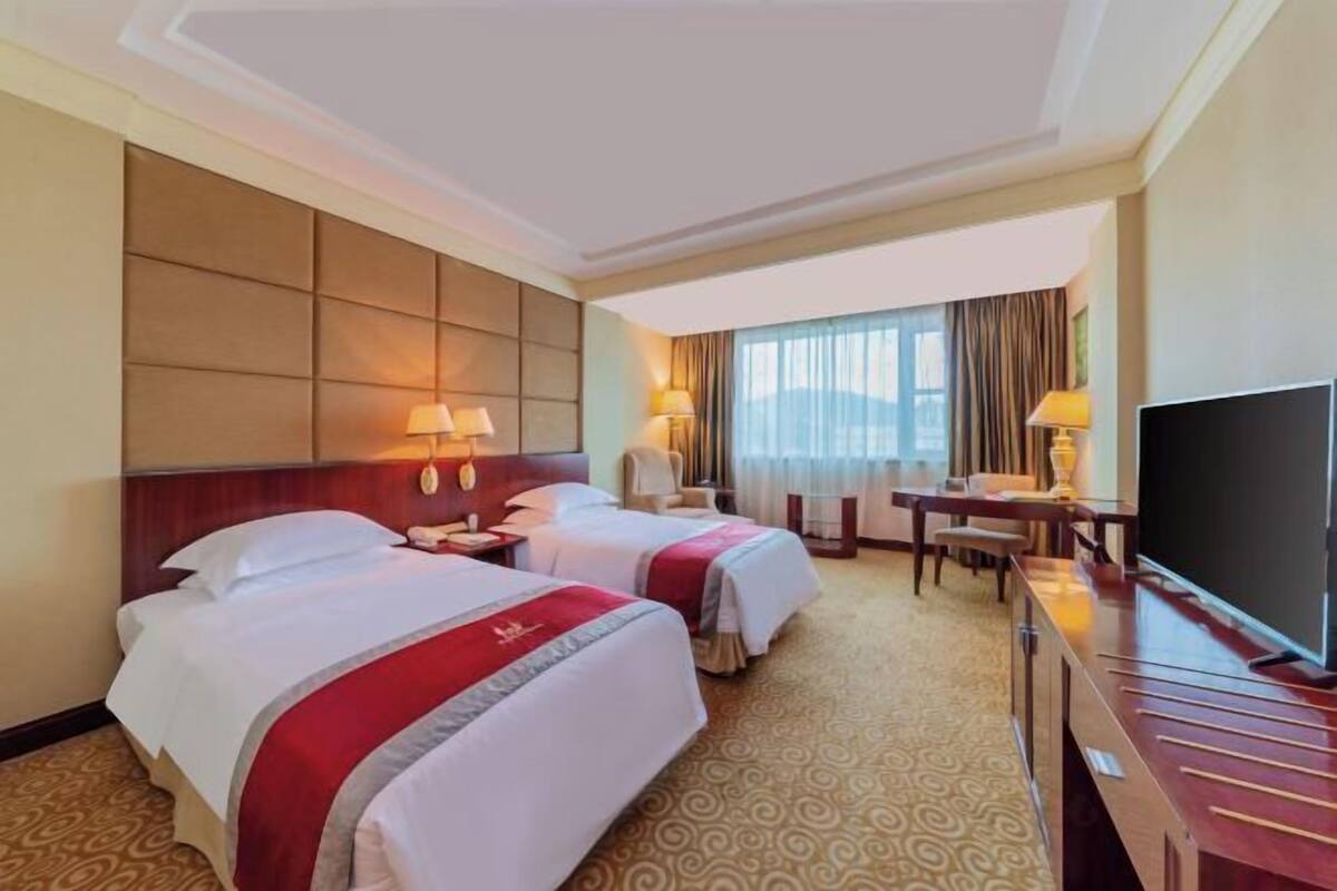 Une chambre d’hôtel avec deux lits, un bureau, une télévision et une vue sur l’extérieur.